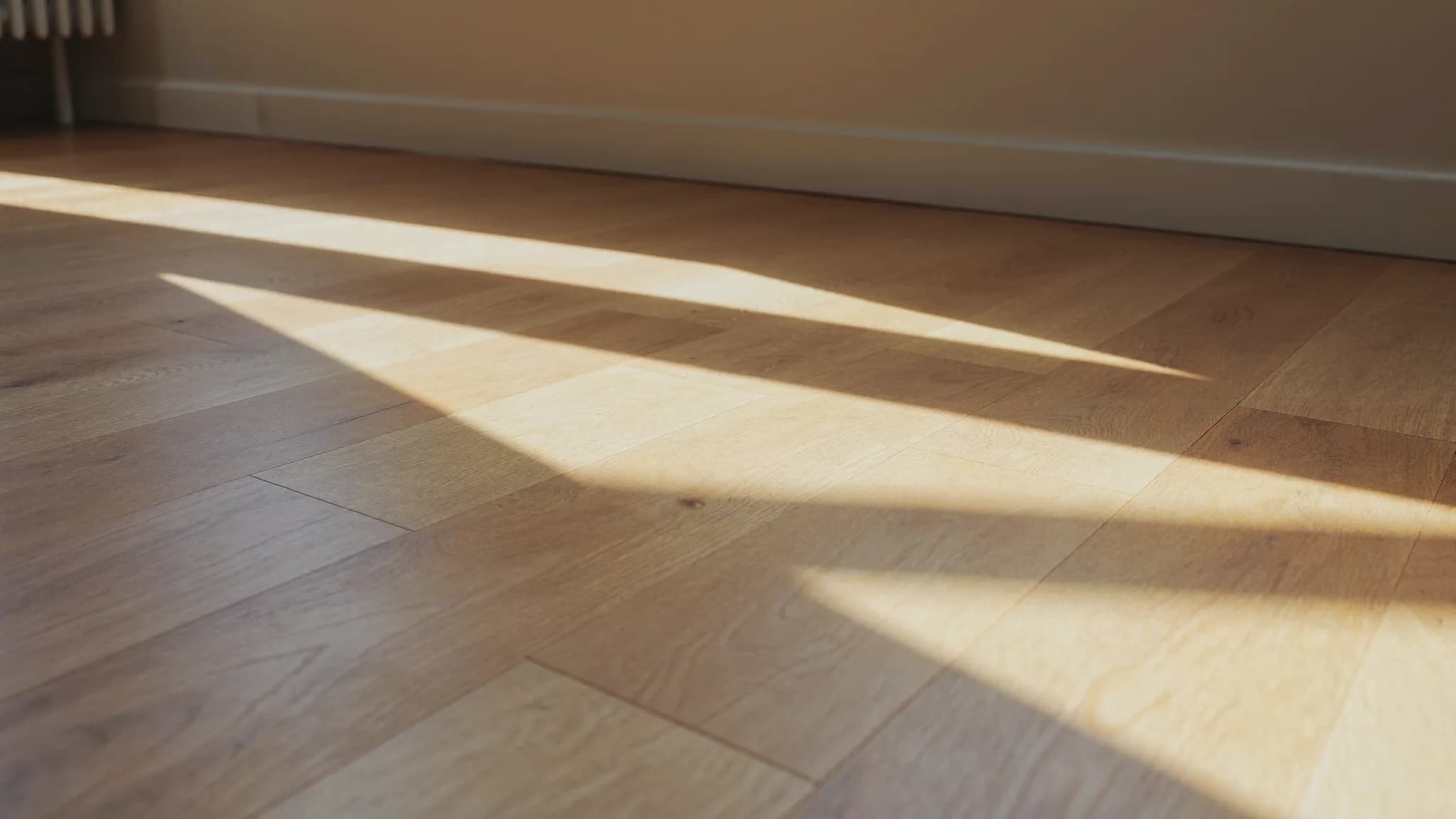 Warm morning sunlight falling in long window-frame shadows across a pale oak floor in an empty apartment