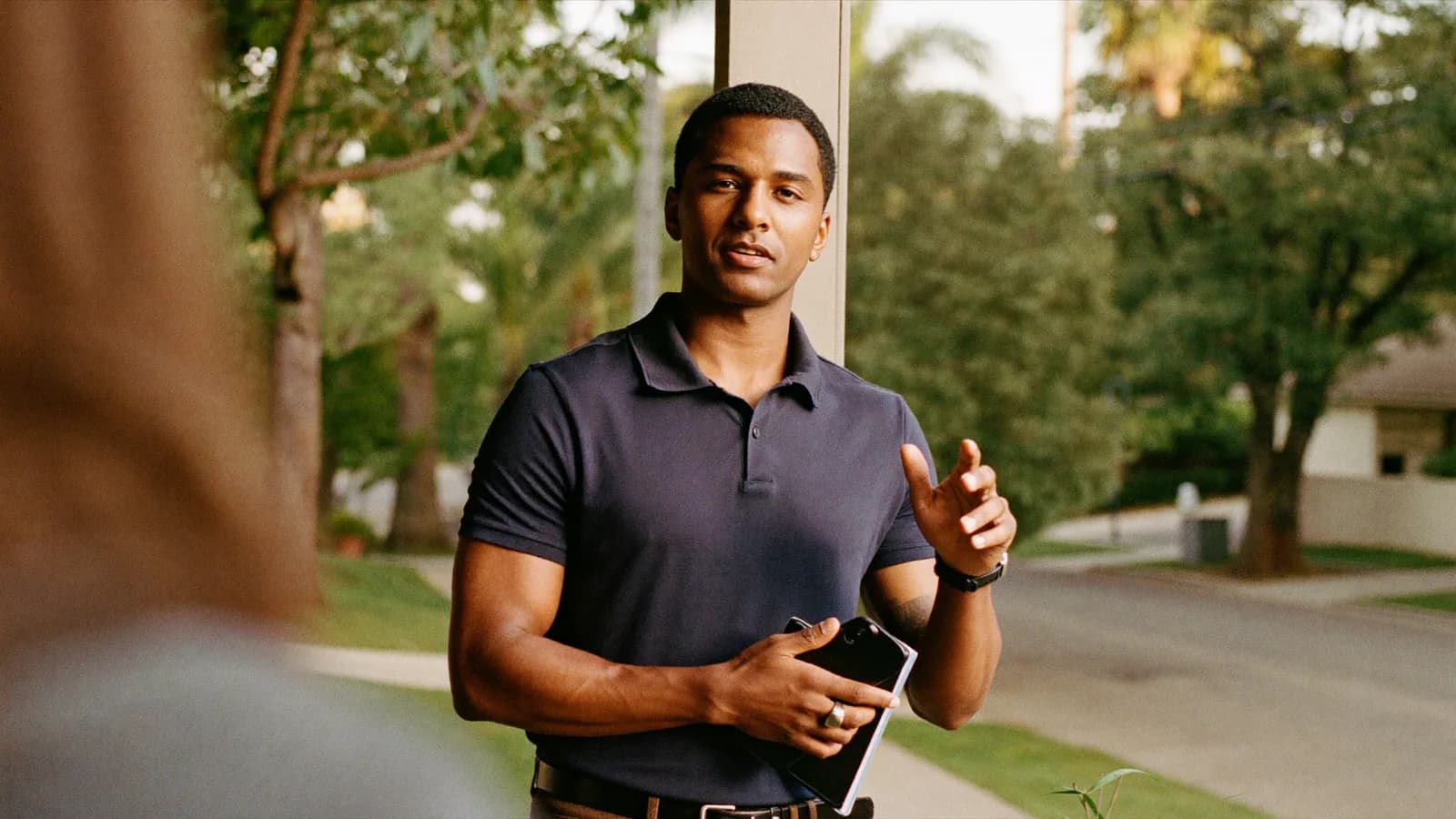 Door-to-door sales rep practicing a pitch on a suburban front porch in warm evening light