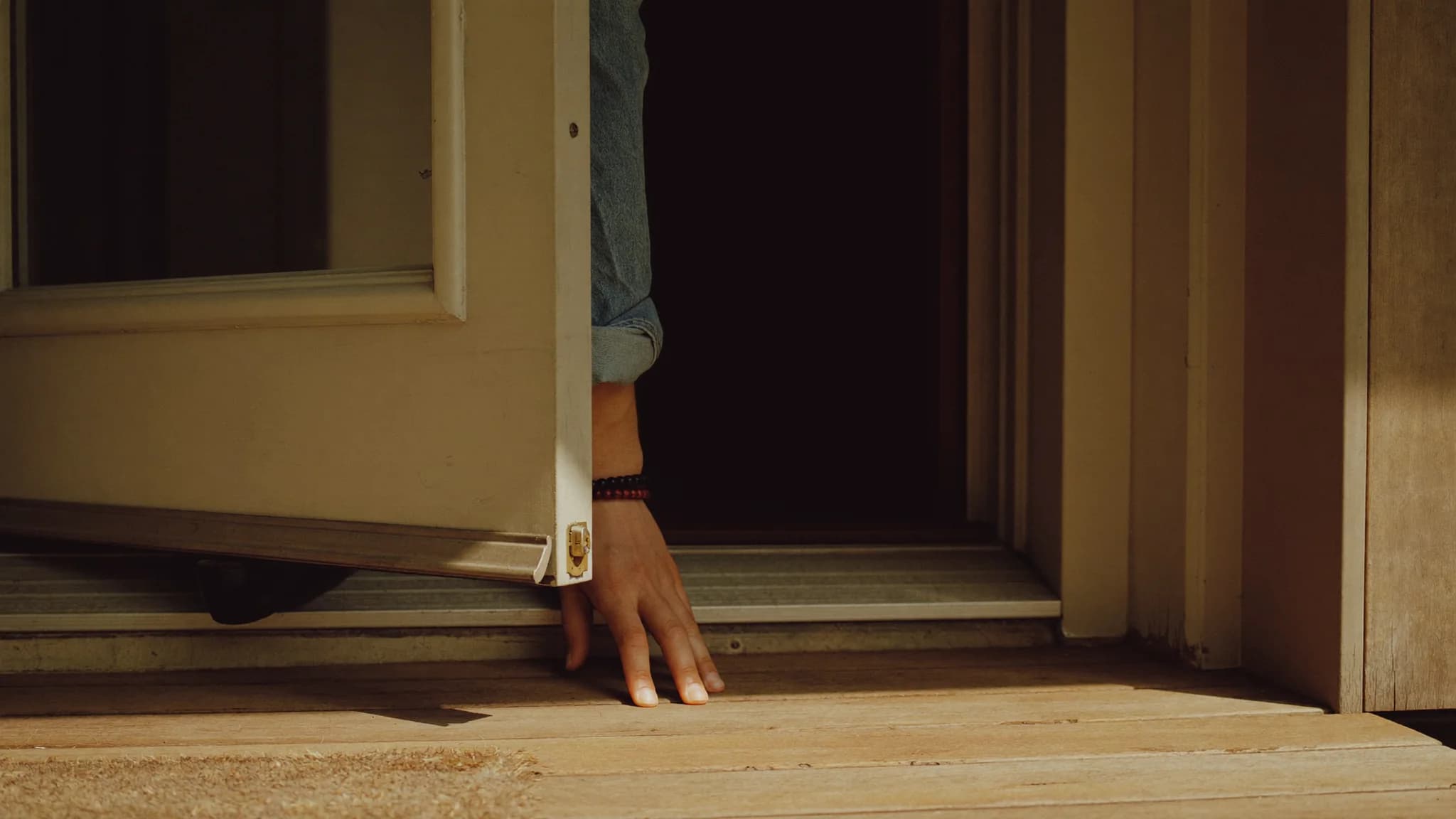 A homeowner's hand resting on the edge of a half open front door, seen from the outside step in warm afternoon light.