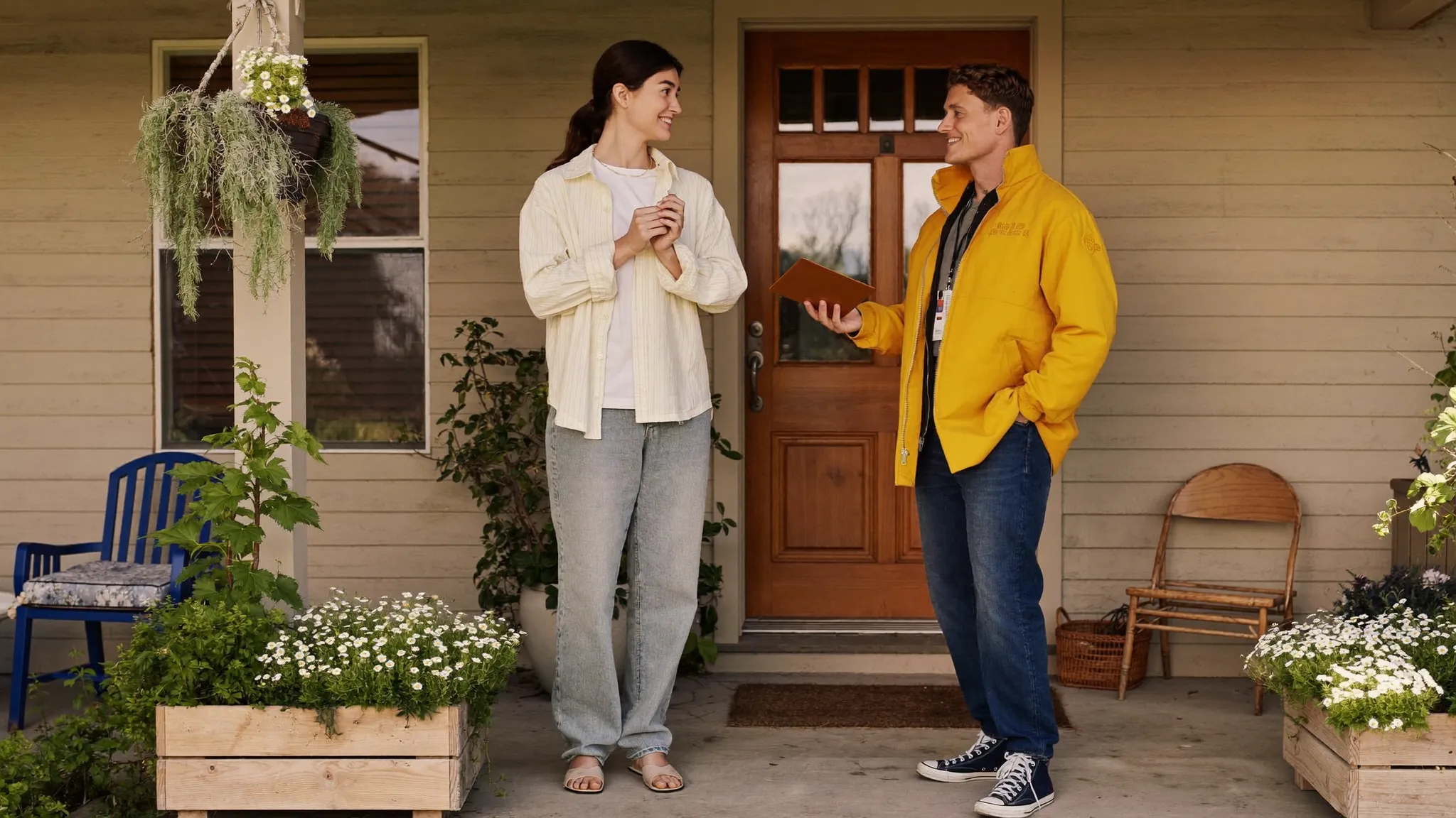 A homeowner and a visiting sales professional talking on a front doorstep in warm afternoon light.
