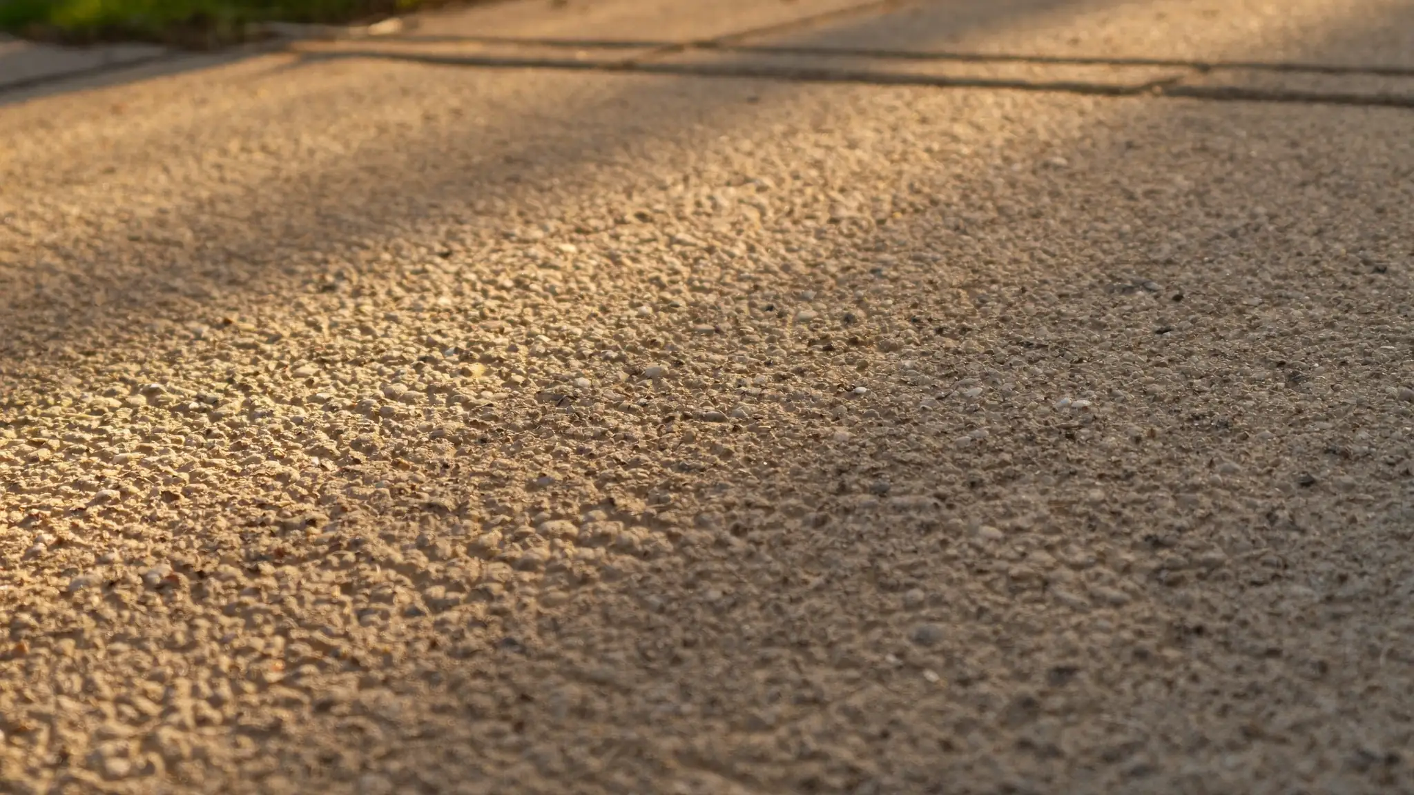 Close-up of a weathered concrete residential driveway with low golden afternoon sunlight raking across the surface