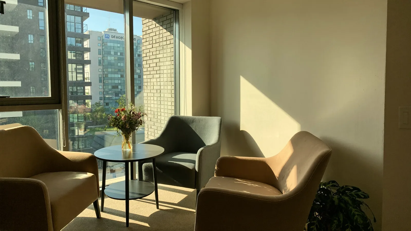 A bright, welcoming apartment leasing office with two chairs beside a large sunlit window.