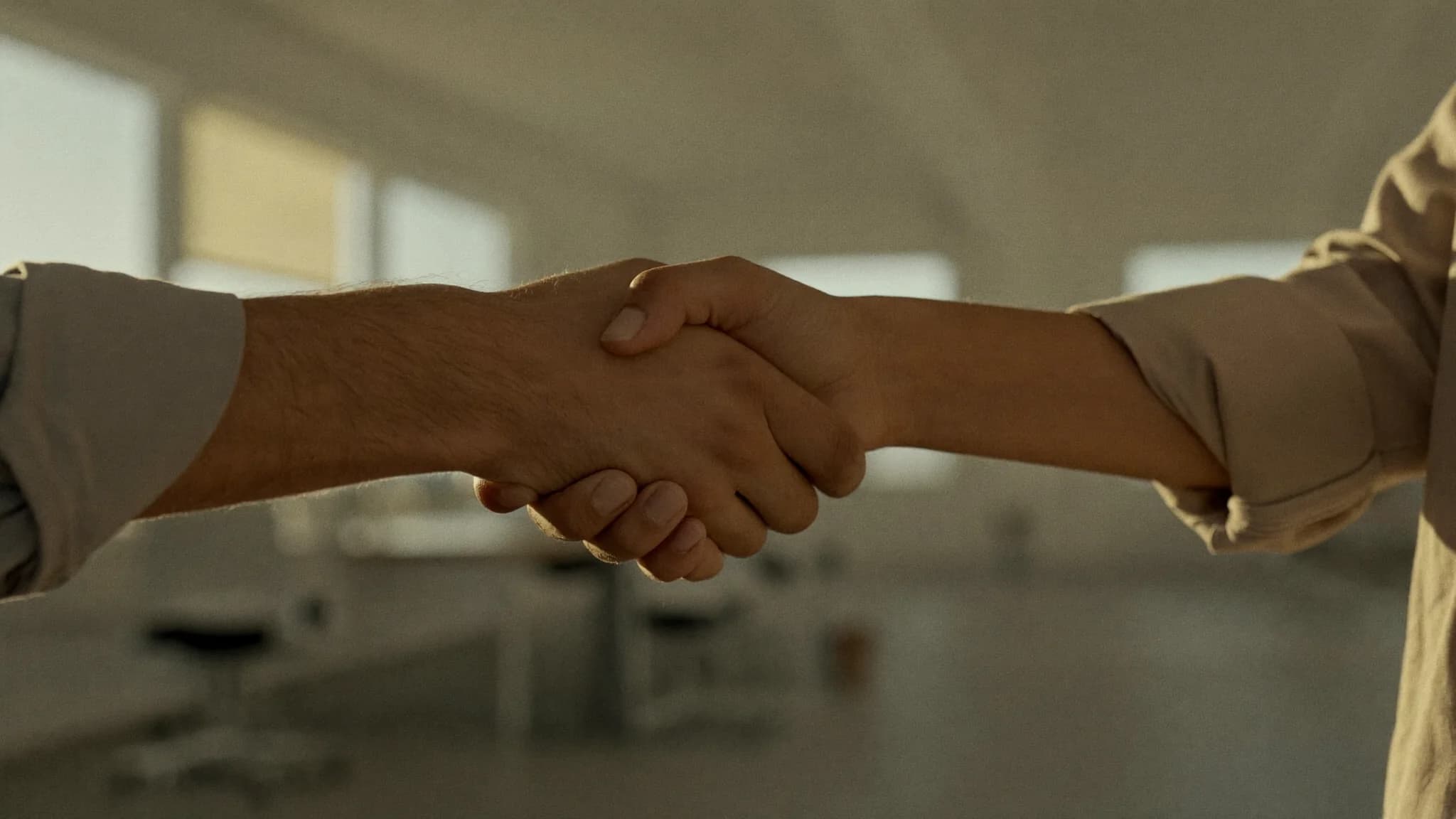 A sales manager welcoming a new sales rep with a handshake in a bright modern office.