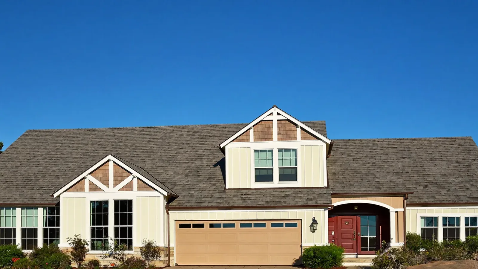 A well-kept suburban home with a brand new asphalt shingle roof under a clear blue sky.