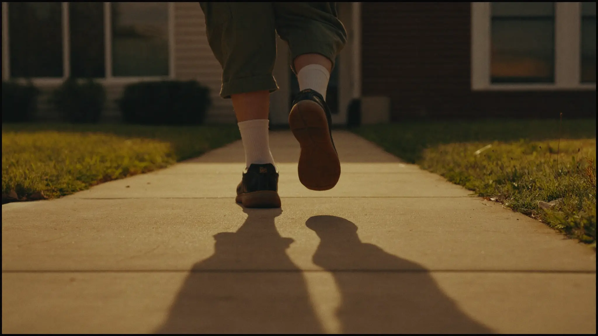 A pest control sales rep walking up a suburban front walkway in morning light, a long shadow stretching ahead on the concrete.