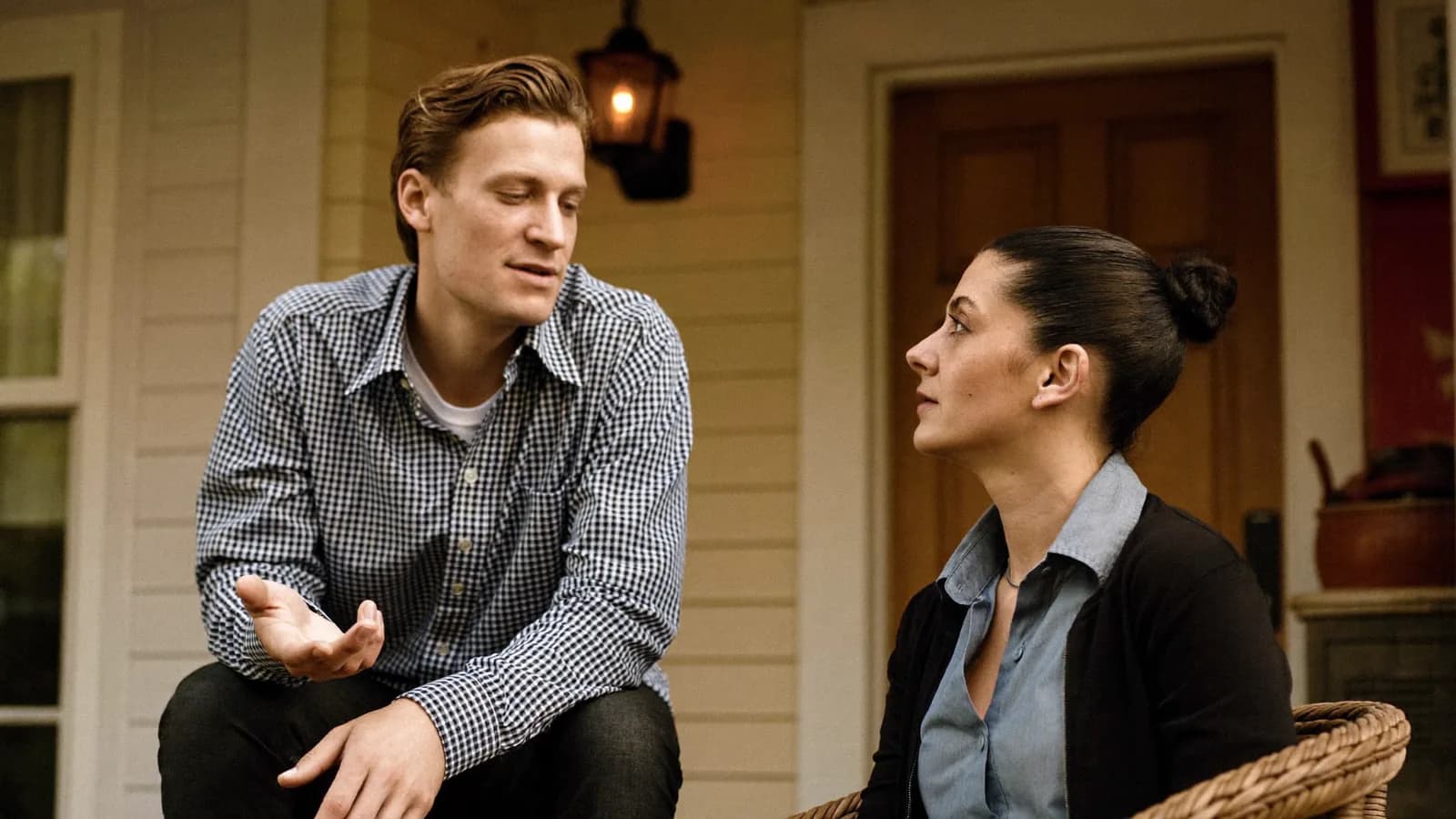 A salesperson listening attentively to a homeowner on a front porch while holding a small notepad in warm daylight.