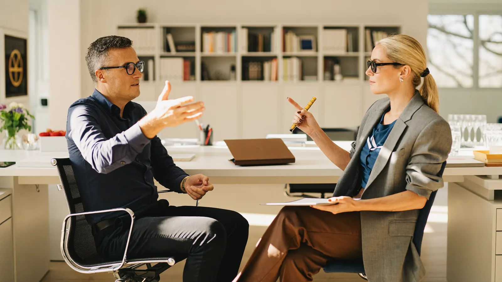 A sales manager and a rep sitting across from each other in a bright office running a practice roleplay.