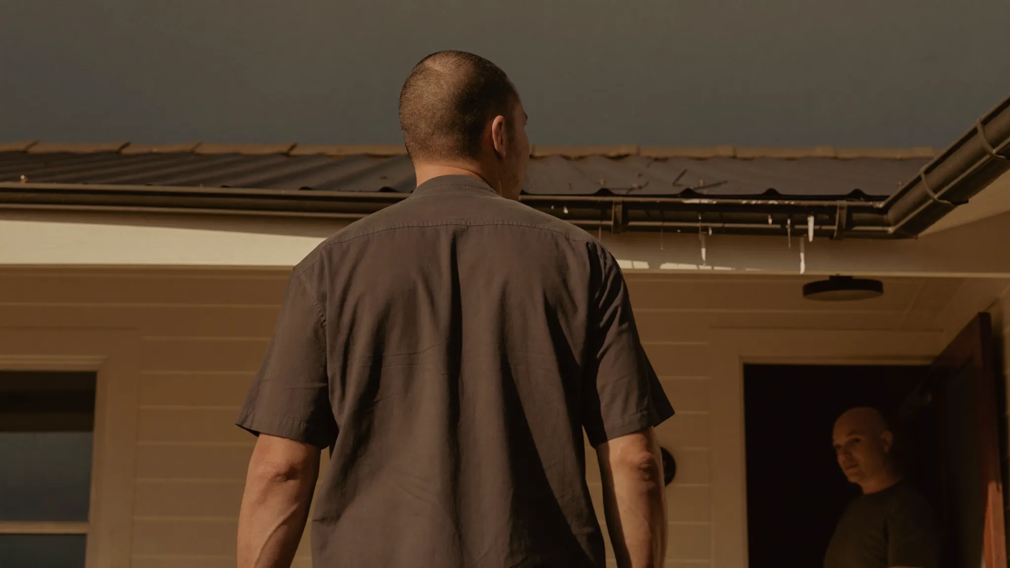 A roofing contractor talking with a homeowner on a front porch under a clearing storm sky.