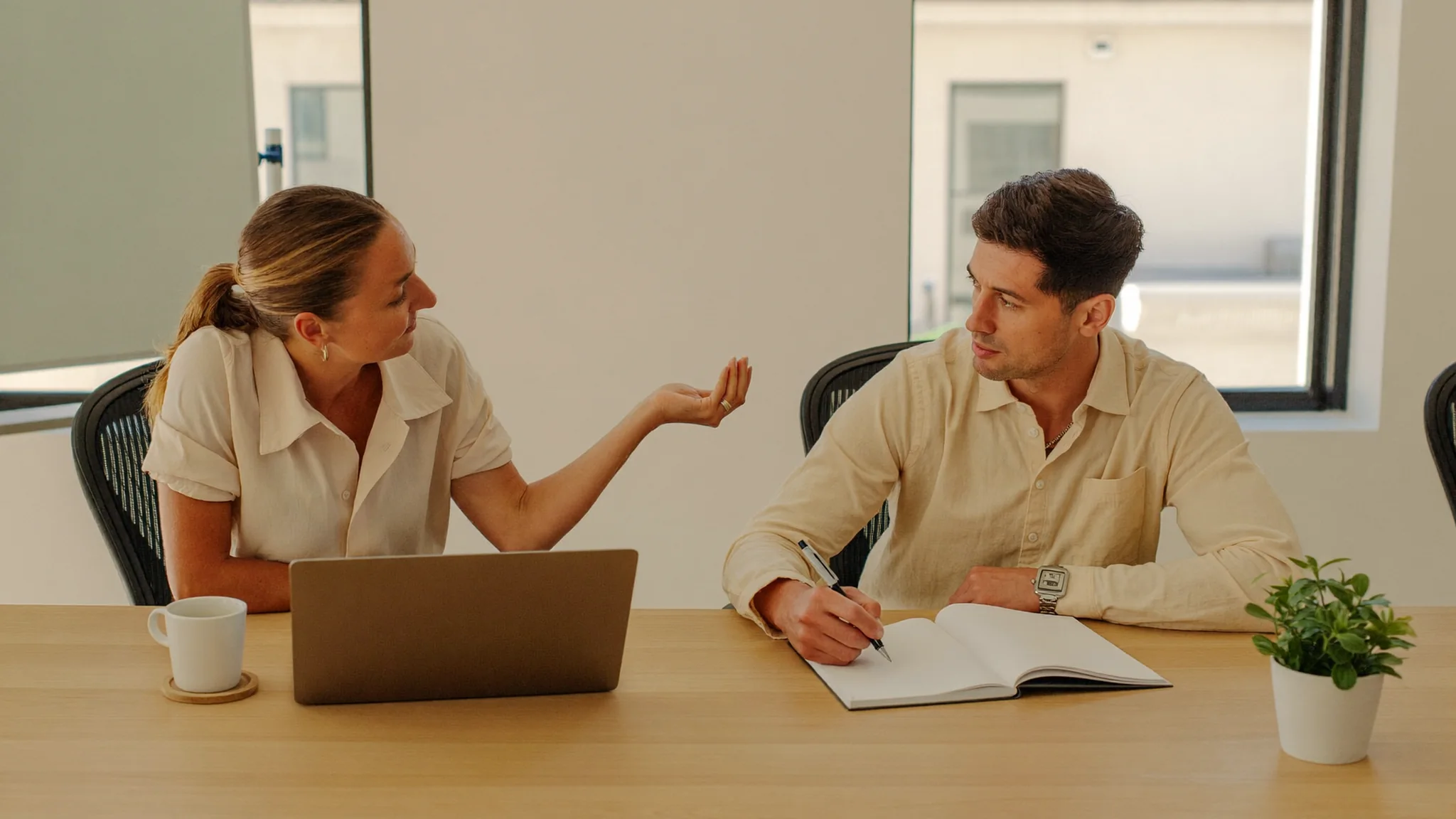 A sales manager and a newly hired rep sitting side by side at a table in a bright office, working through an onboarding plan together.
