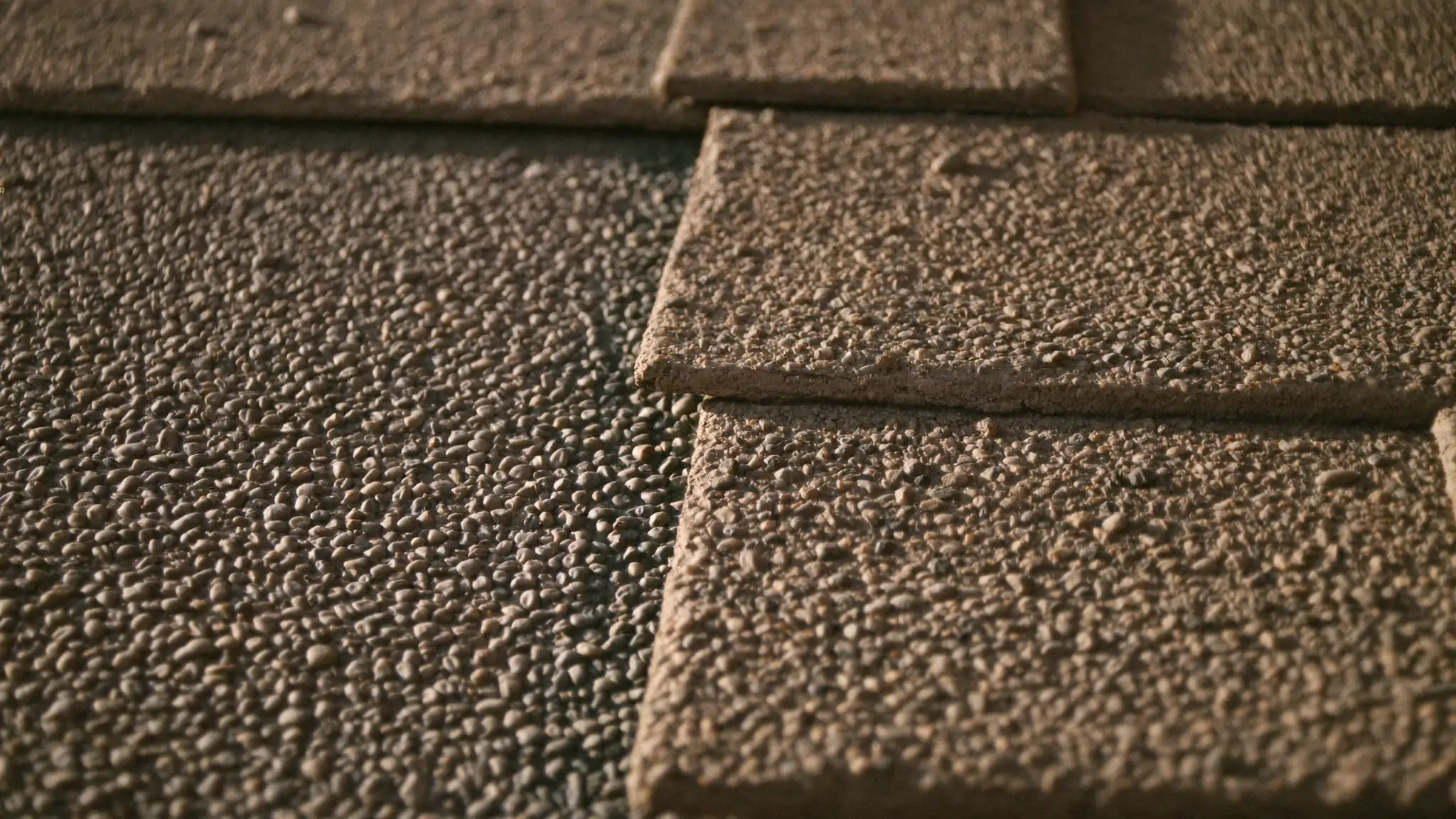 Close-up of overlapping asphalt roofing shingle courses and mineral granules in warm raking light