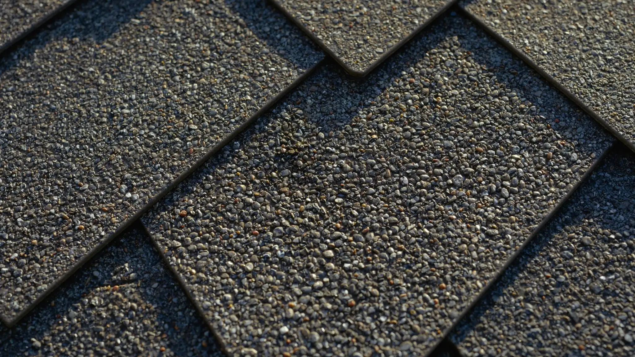 Extreme close-up of asphalt shingle granules showing hail impact marks in raking light