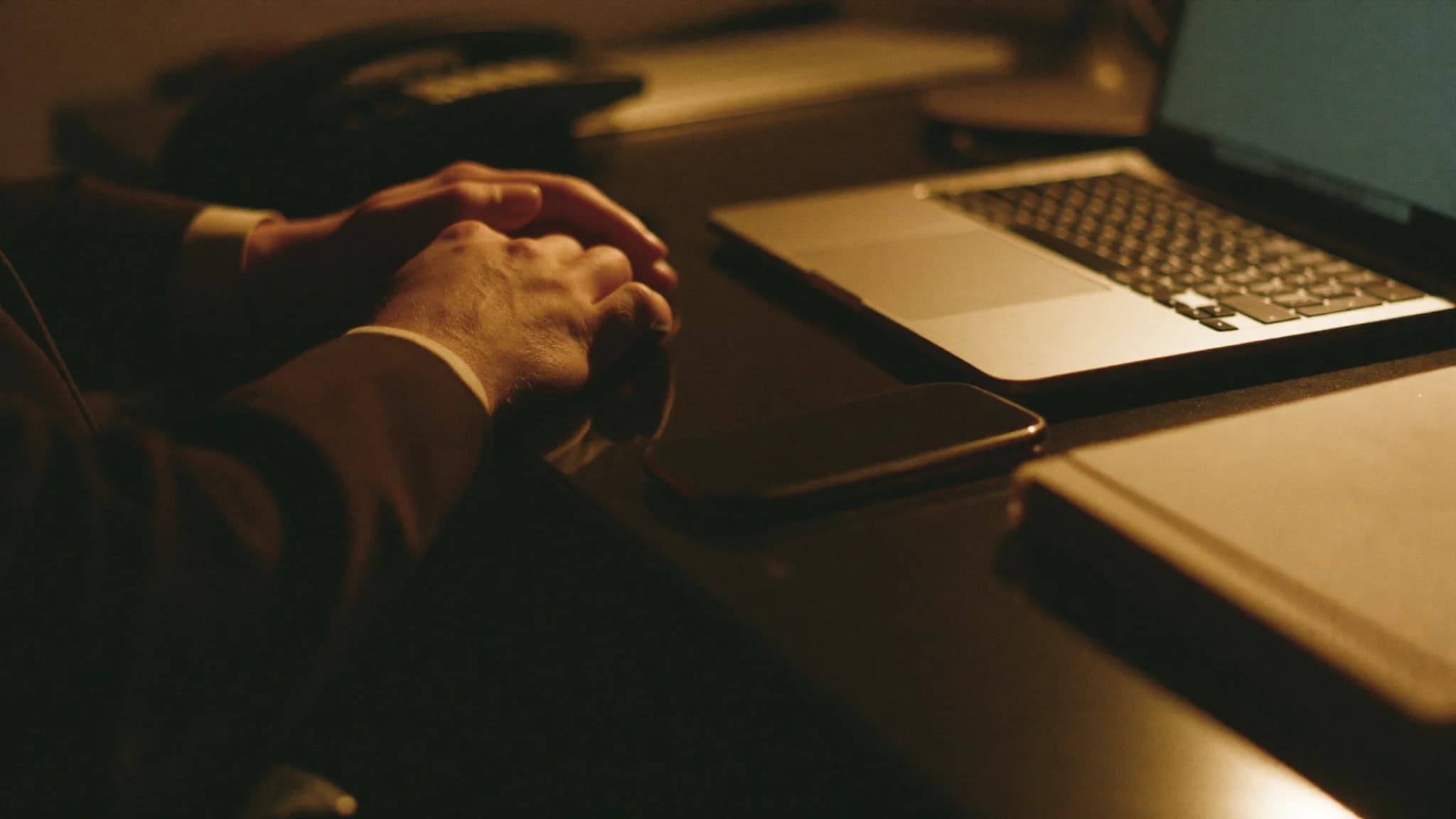 A sales manager's hands on a desk beside a phone and a closed laptop in warm evening light.