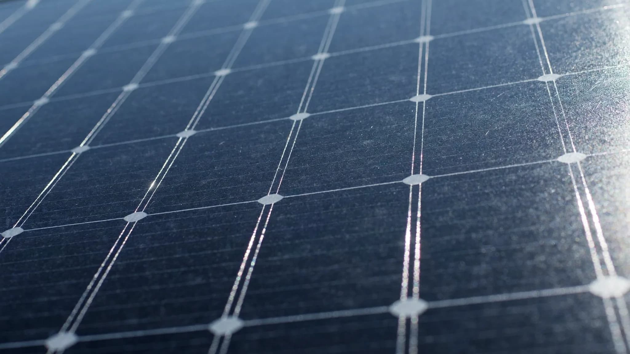 Extreme close-up of solar panel cells at an angle with sunlight glare across the surface