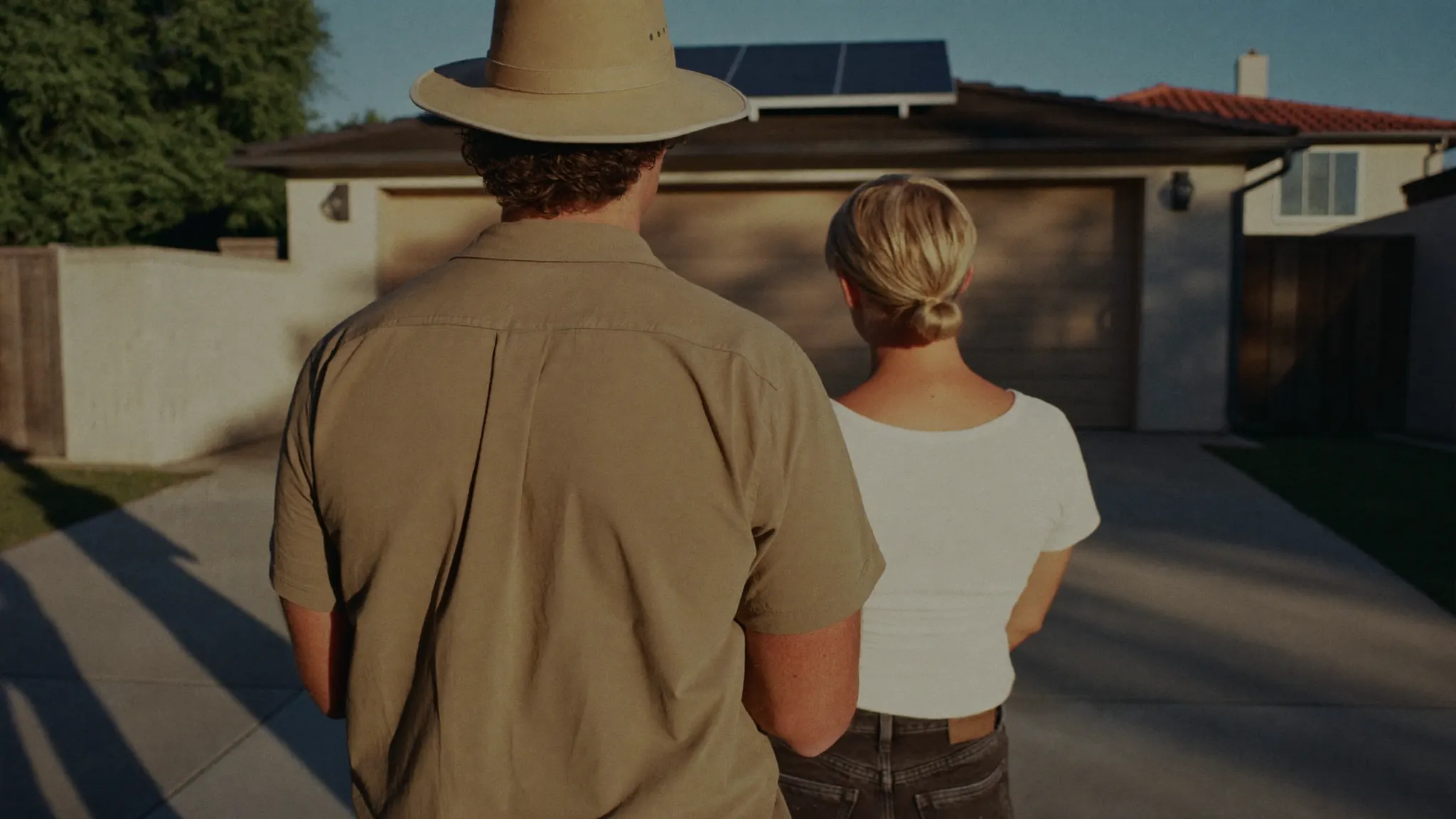 A solar sales rep and a homeowner standing in a driveway looking up toward the roofline in warm afternoon light.