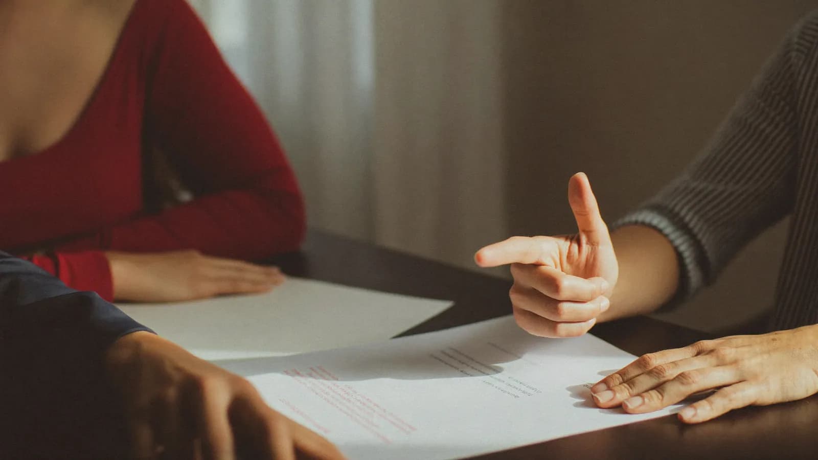 Two people at a table in warm window light, one nodding in agreement over a document, reaching a yes.